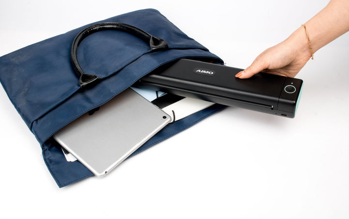 Aimo Bluetooth A4 thermal printer being placed into a blue bag next to a tablet and notebook